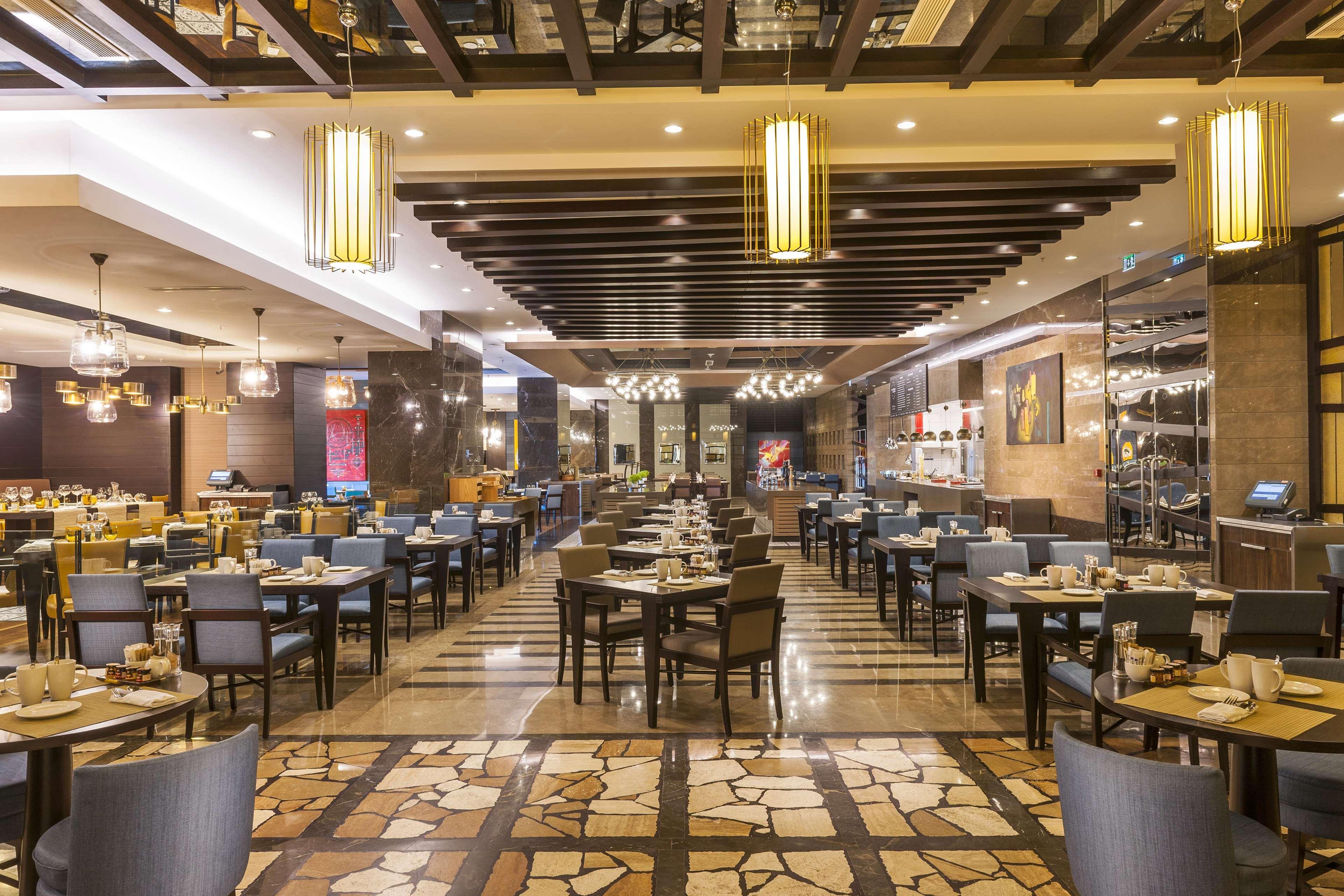 Radisson Blu Hotel, Istanbul Sisli Exterior photo The photo shows a spacious and elegantly designed restaurant. It features multiple dining tables arranged neatly throughout the room. The decor includes modern lighting fixtures, wooden ceiling beams, and a mix of light and dark materials on the wall