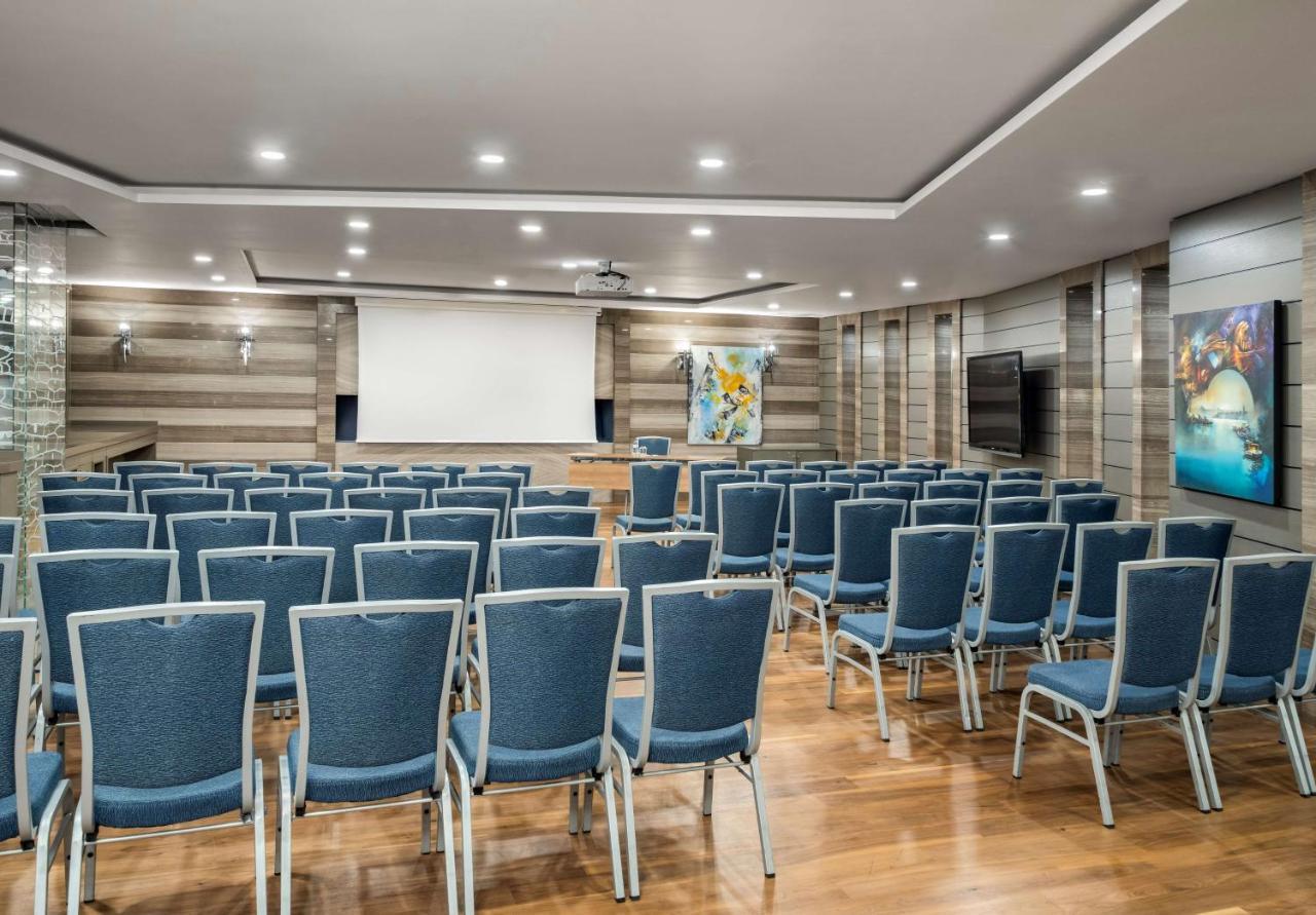 Radisson Blu Hotel, Istanbul Sisli Exterior photo The photo shows a spacious conference room set up for a meeting or presentation. There are rows of blue chairs arranged neatly in front of a large blank screen at the front of the room. The room features wooden flooring and walls with a modern design